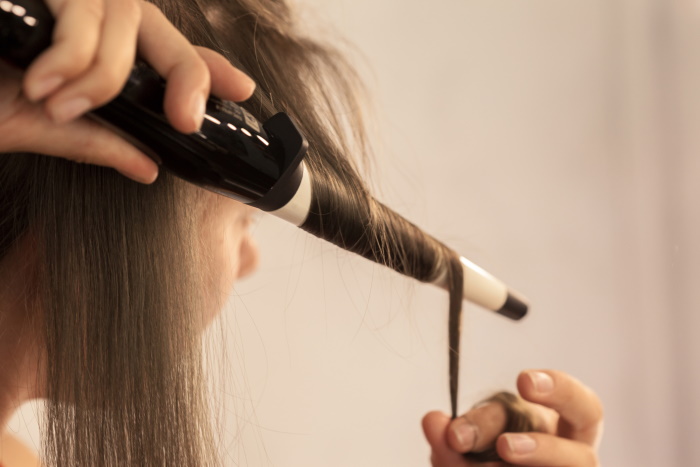 Hairstylist curling hair client in hairdressing salon